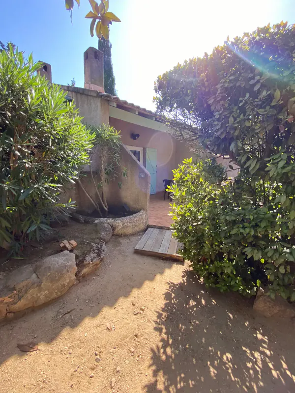 L’entrée de la maison, volets bleus et terrasse ombragée par la végétation